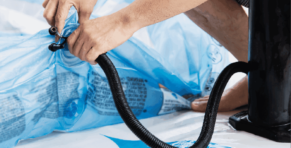 A close-up of hands wrapping or organizing a coiled black garden hose with blue plastic bag or tarp in the background during daytime.